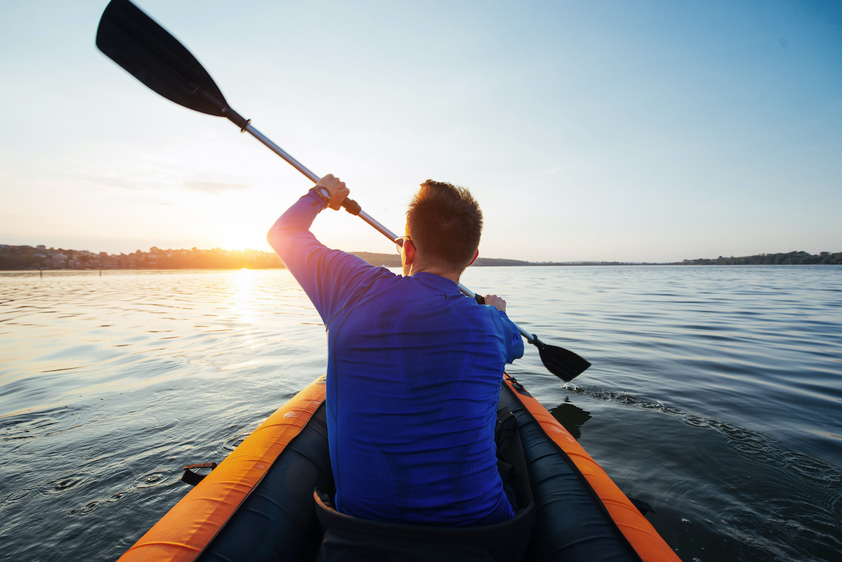 man floating on lake in a kayak at fantastic sunset.
