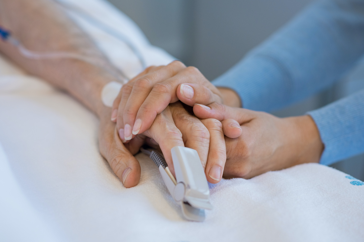 Daughter holding the hand of an elderly father. Closeup of woman holding senior man hand in hospital. Close up of nurse holding old man hand with oxygen saturated probe on finger.