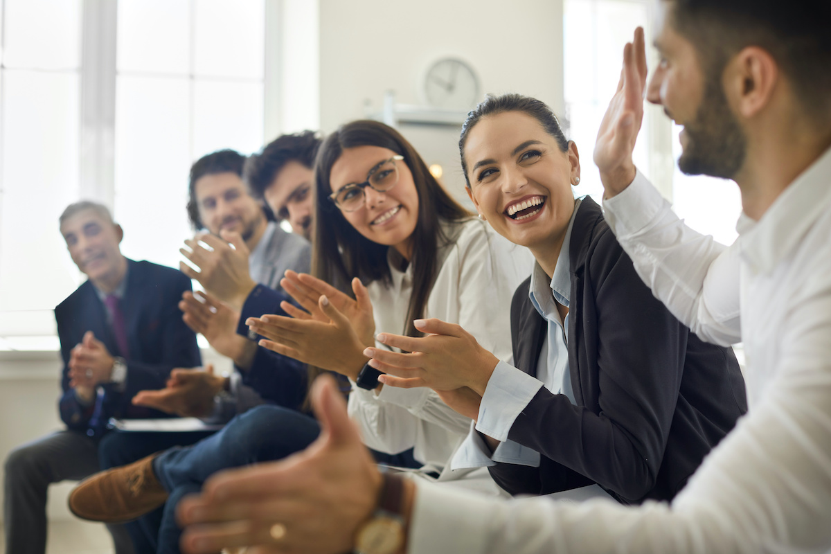 Happy business professionals applauding colleague in presentation or corporate meeting
