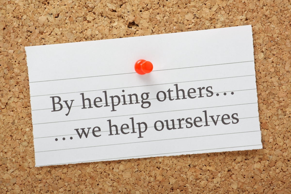 a corkboard with the message by helping others we help ourselves pinned to it